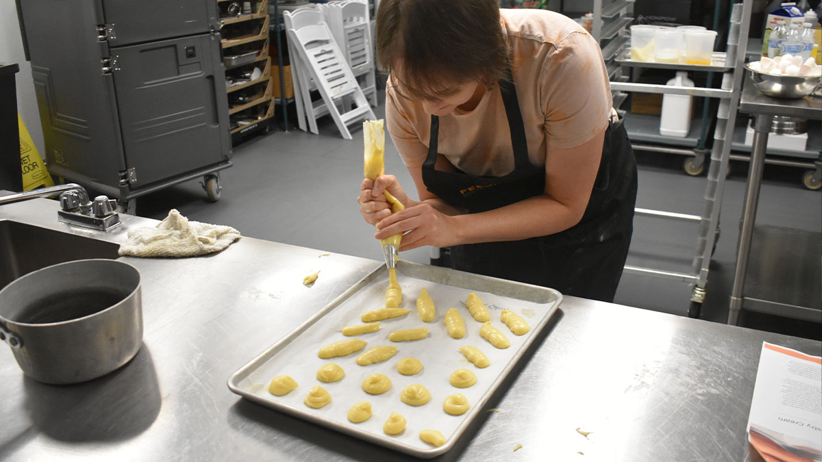 Woman piping cookies on a baking sheet.